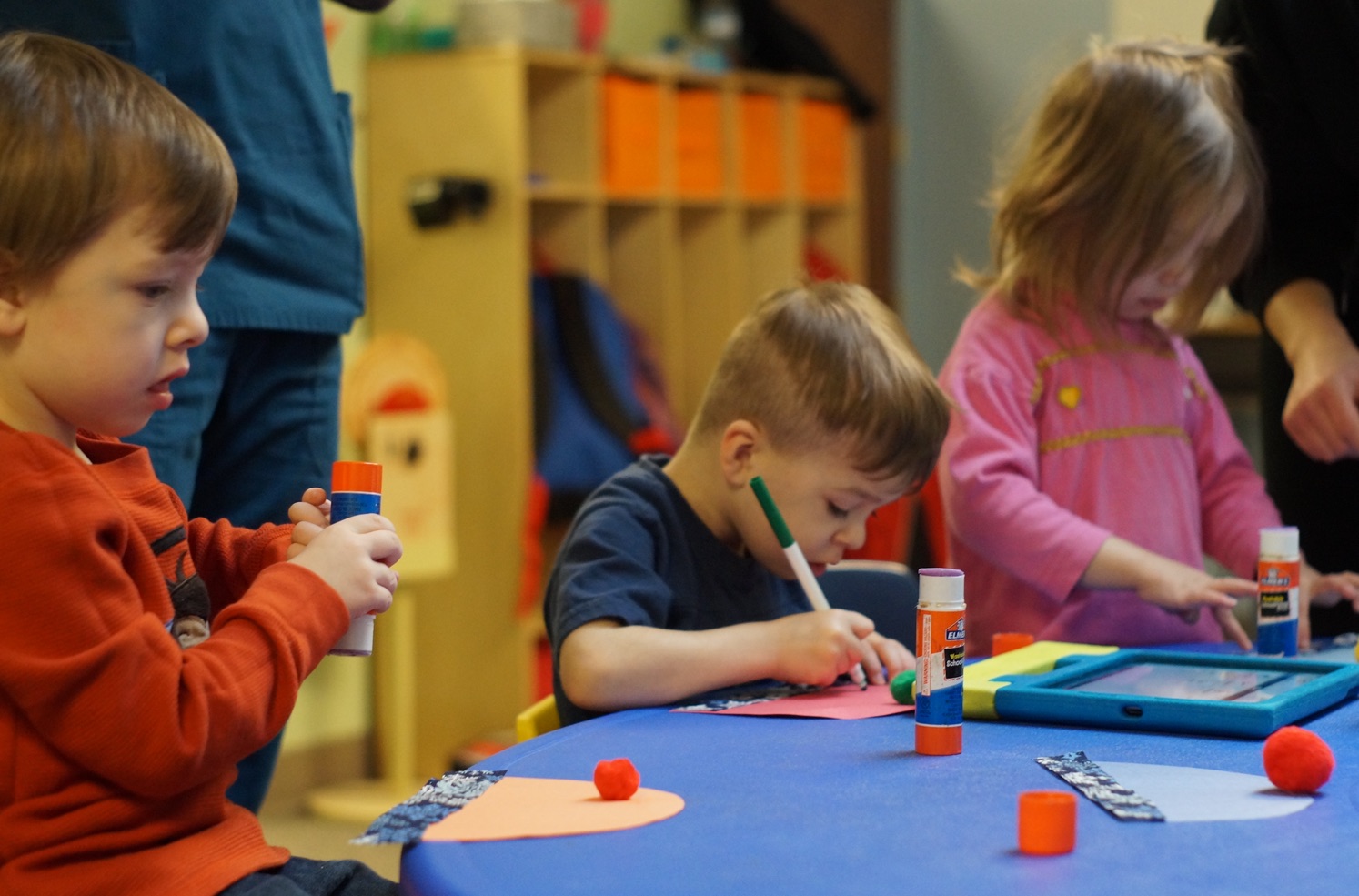 Children at a table doing crafts with glue, markers, and construction paper